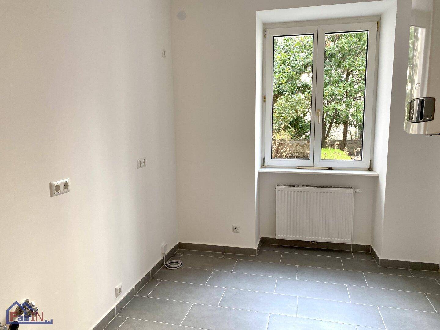Heller Raum mit Fliesenboden und Fenster, vorbereitet für die Installation einer Küche.