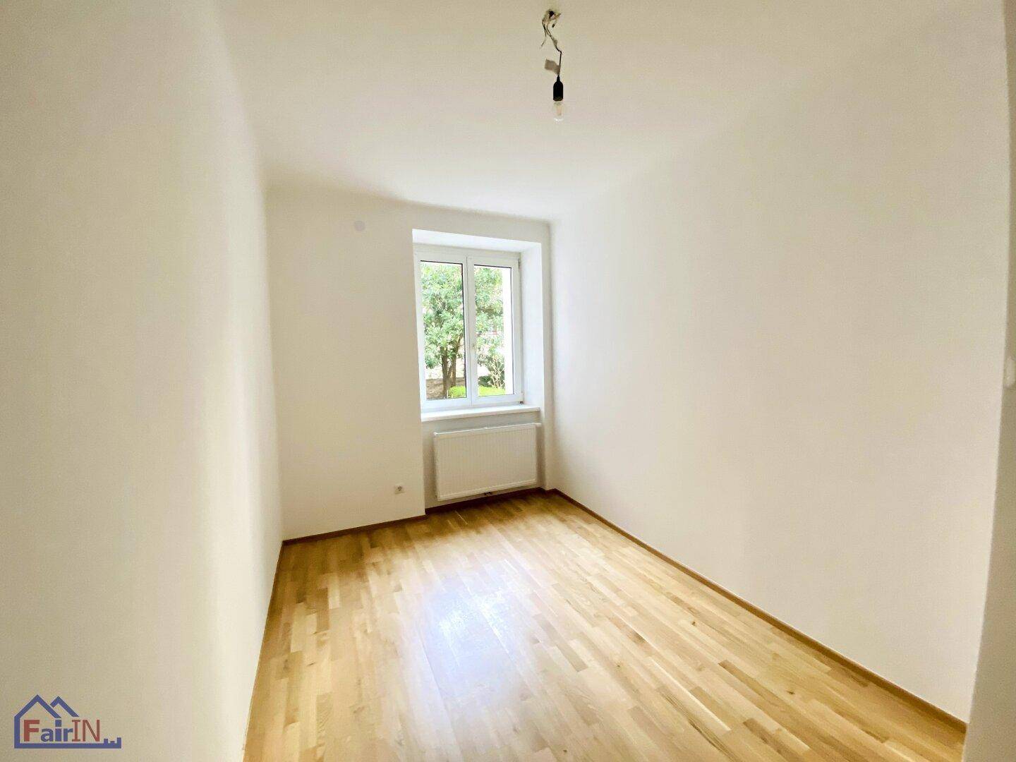 Lichtdurchflutetes Zimmer mit Parkettboden und Blick ins Grüne durch das Fenster.