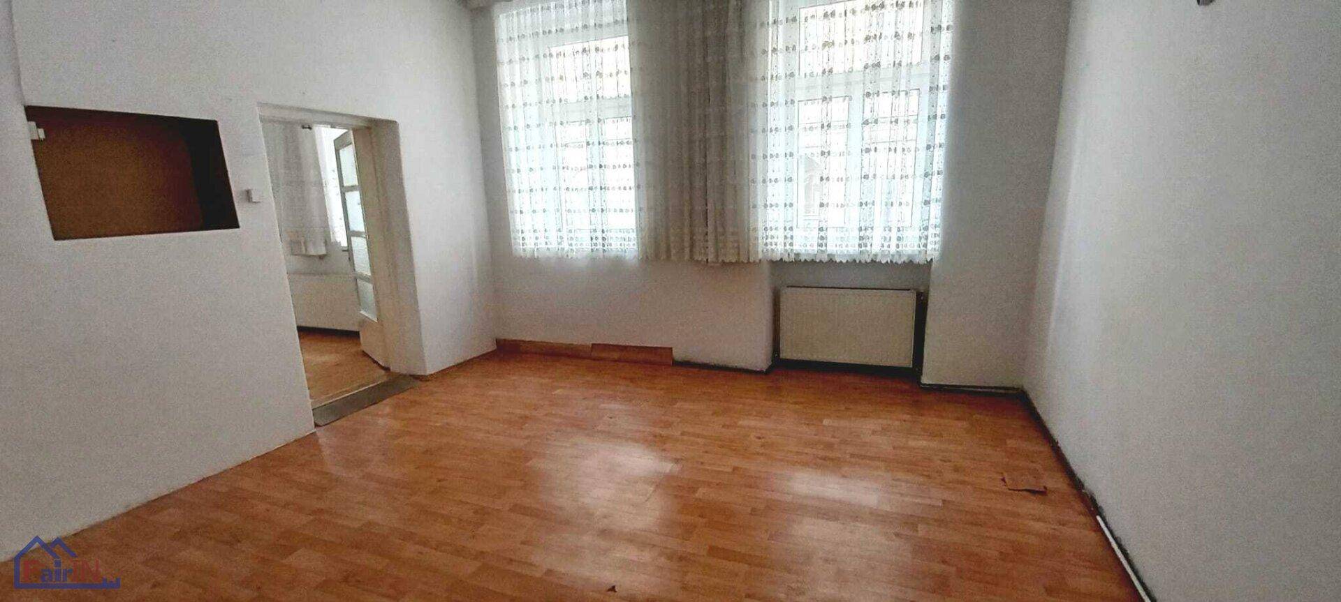 Leeres Zimmer mit hellem Holzfußboden und zwei Fenstern, bereit zur Einrichtung.