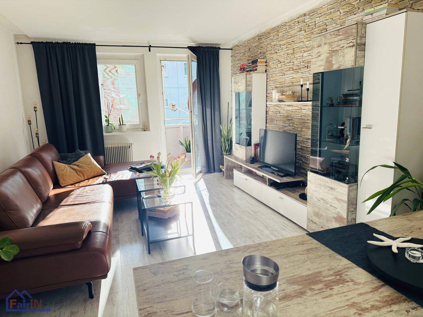 Helles Wohnzimmer mit bequemer Ledercouch, dekorativer Steinwand und Zugang zum Balkon.