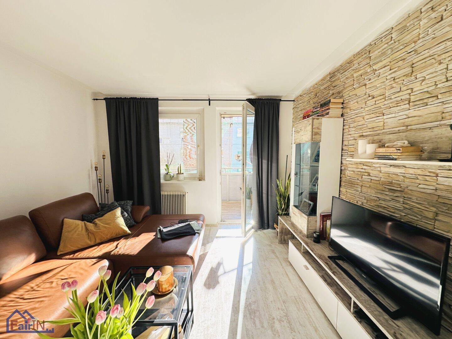 Sonniges Wohnzimmer mit Ledersofa, dekorativer Steinwand und direktem Balkonzugang.