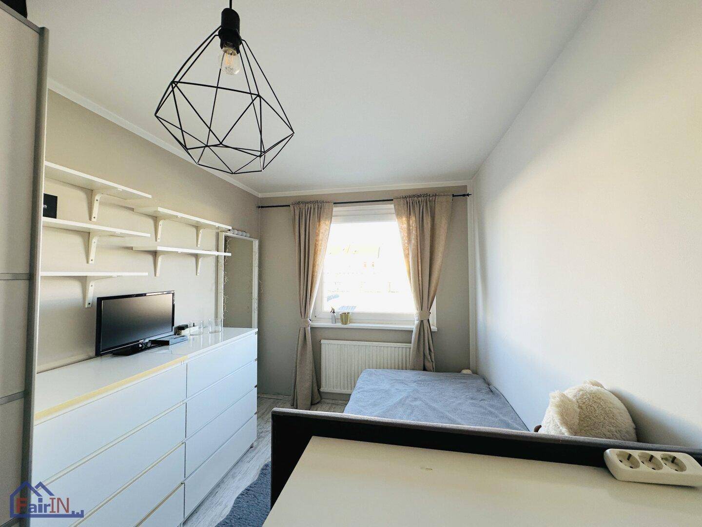 Helles Schlafzimmer mit Einzelbett, Kommode und Fenster mit Vorhängen für Privatsphäre.