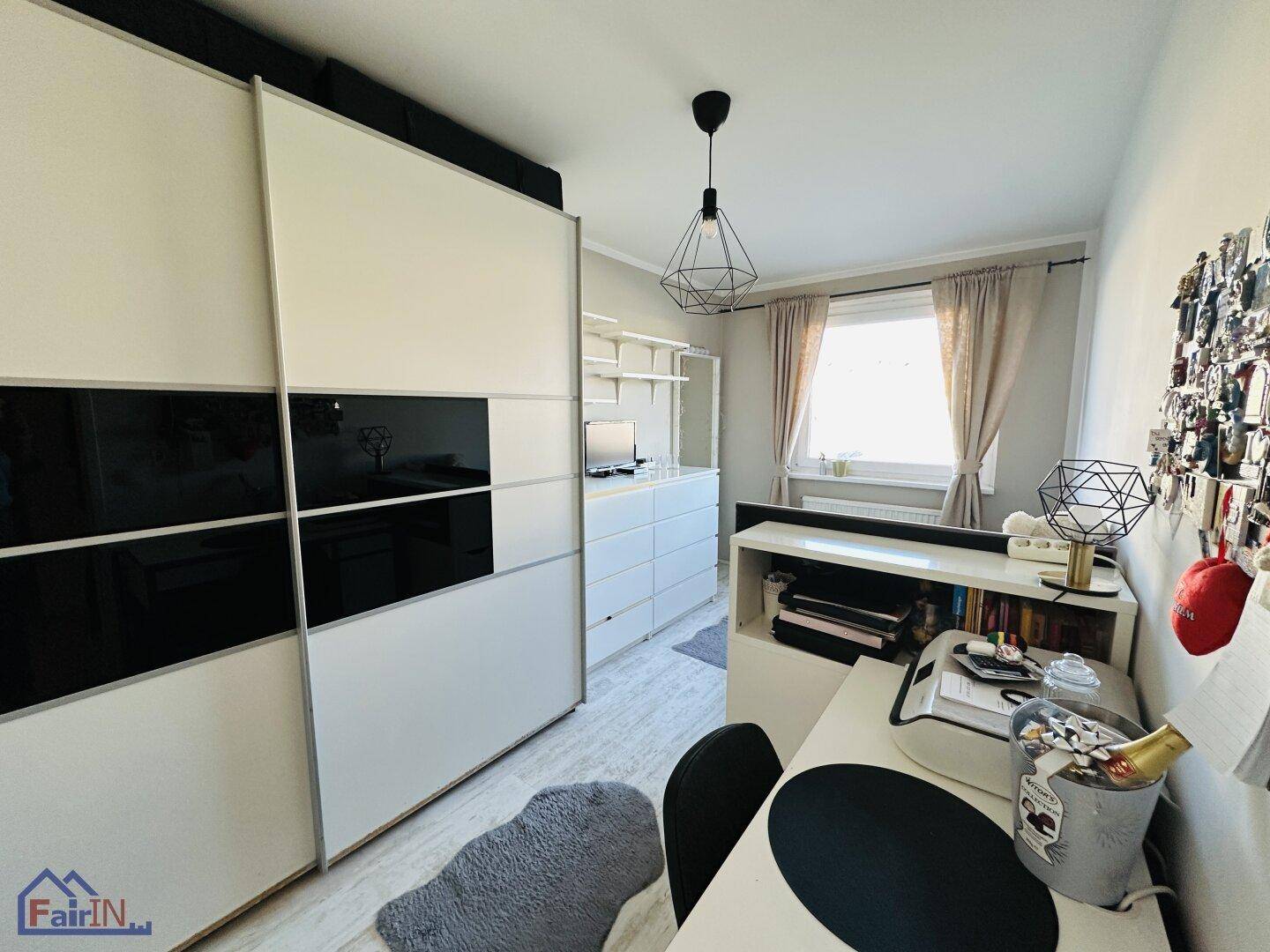Schlafzimmer mit großem Schiebetürenschrank, Schreibtisch und Fenster für Tageslicht.