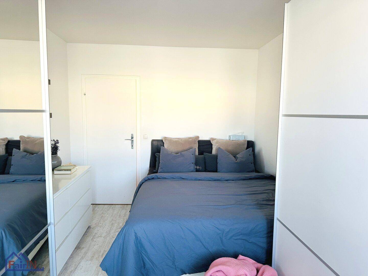 Helles Schlafzimmer mit Doppelbett, Spiegelschrank und weißer, moderner Einrichtung.