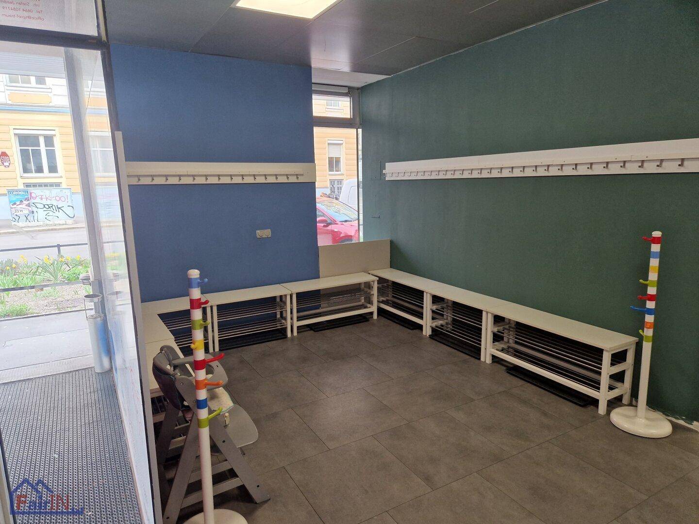 Eingangsbereich mit Garderobenleisten und Sitzbänken, ideal für Kinder, mit Blick auf die Straße.