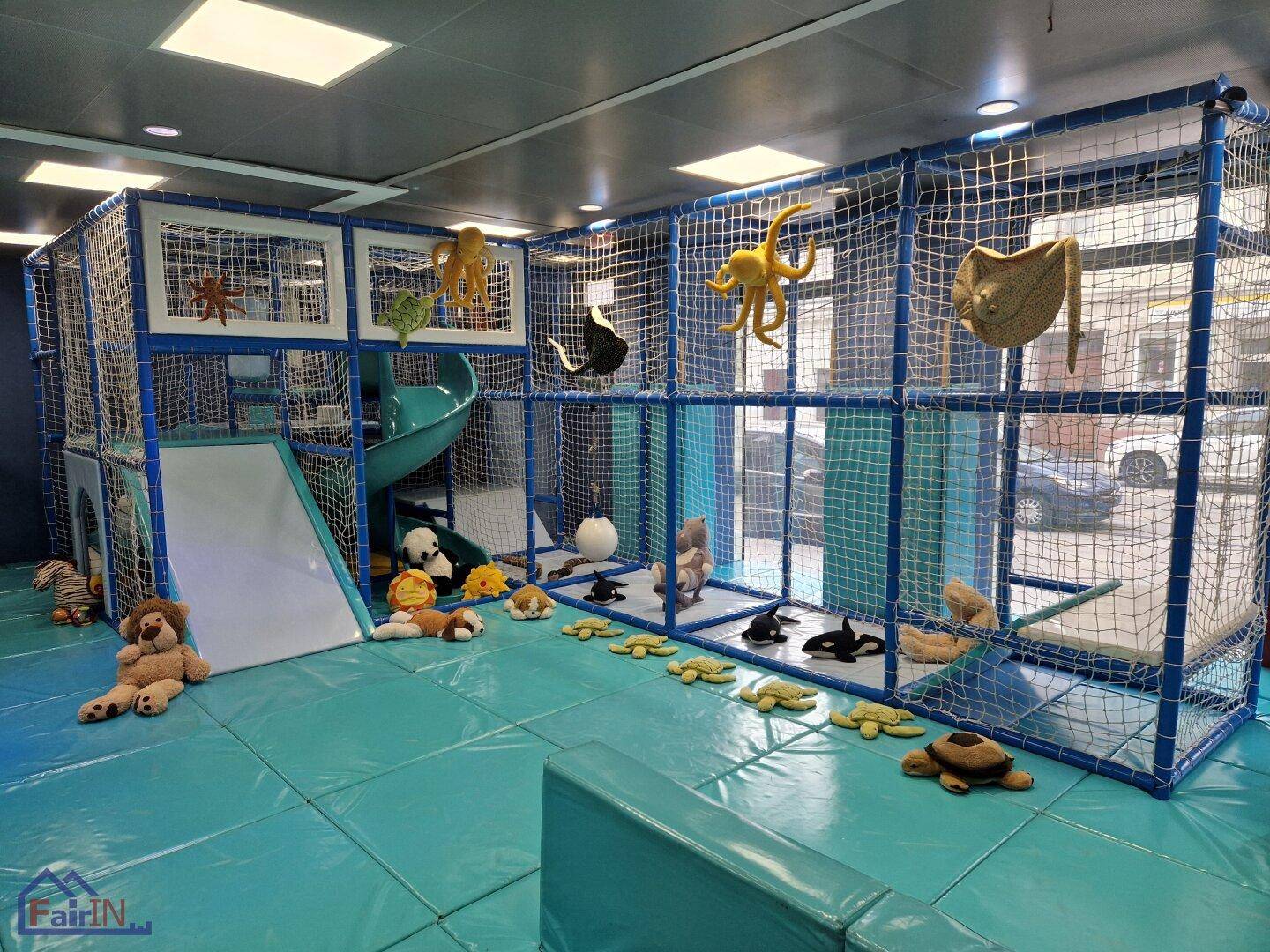 Indoor-Spielplatz mit Kletternetz, Rutsche und Meerestier-Dekoration, auf weichem, blauem Boden.