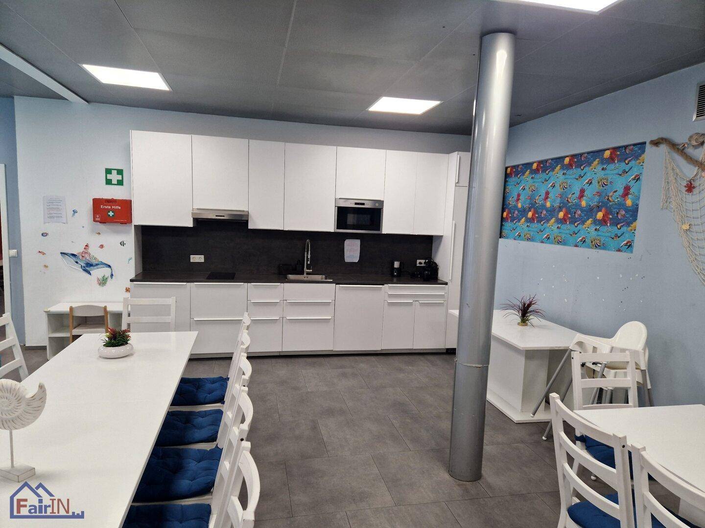 Moderne Küche mit weißen Schränken und dunkler Arbeitsplatte, integriert in einen Essbereich mit maritimer Dekoration.