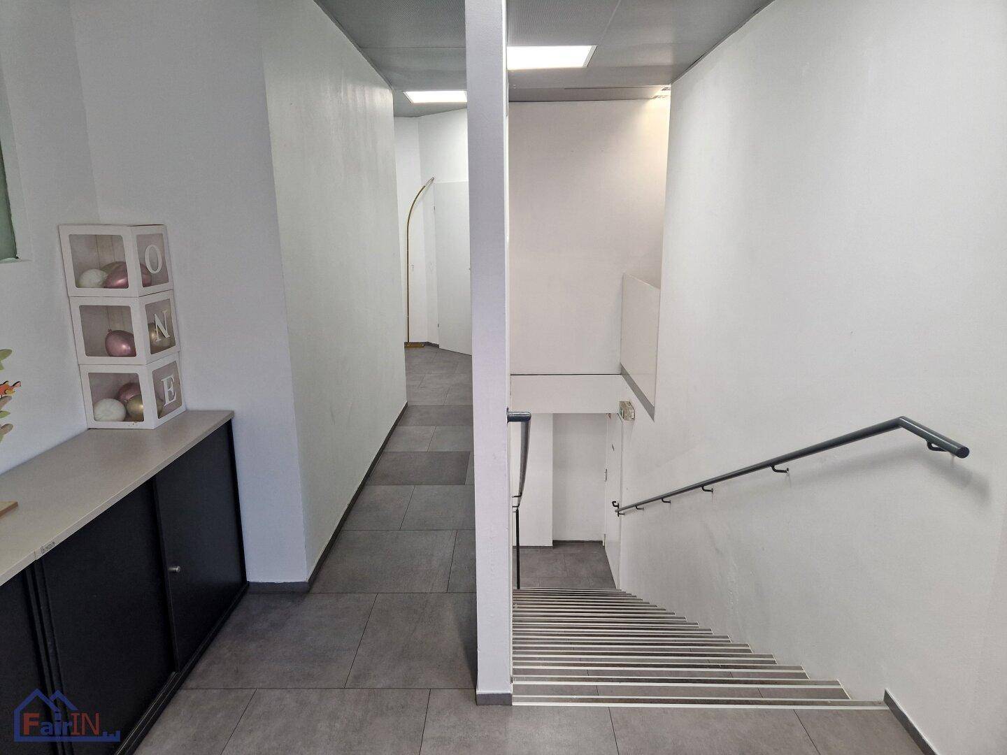 Heller Flur mit Treppenhaus und Handlauf, der zu weiteren Bereichen des Gebäudes führt.
