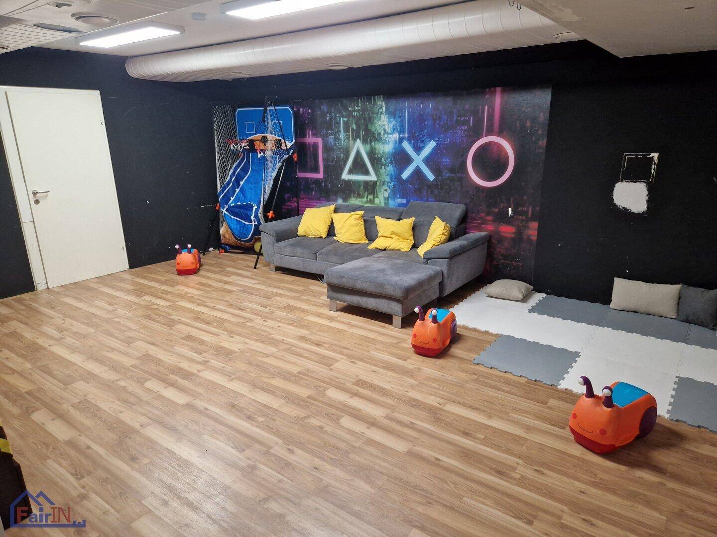 Gemütlicher Loungebereich mit großem Sofa und Spielkonsolen-Wanddekoration, auf Holzboden.