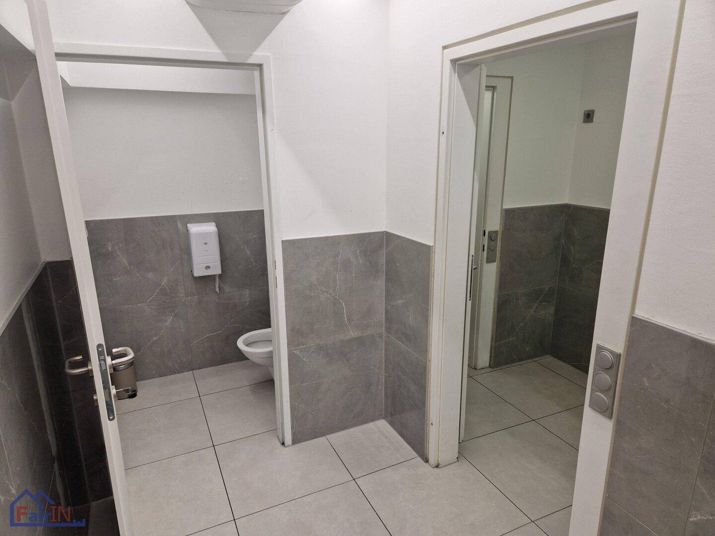 Toilettenbereich mit grauen Fliesen und weißer Wand, ausgestattet mit einem wandhängenden WC.
