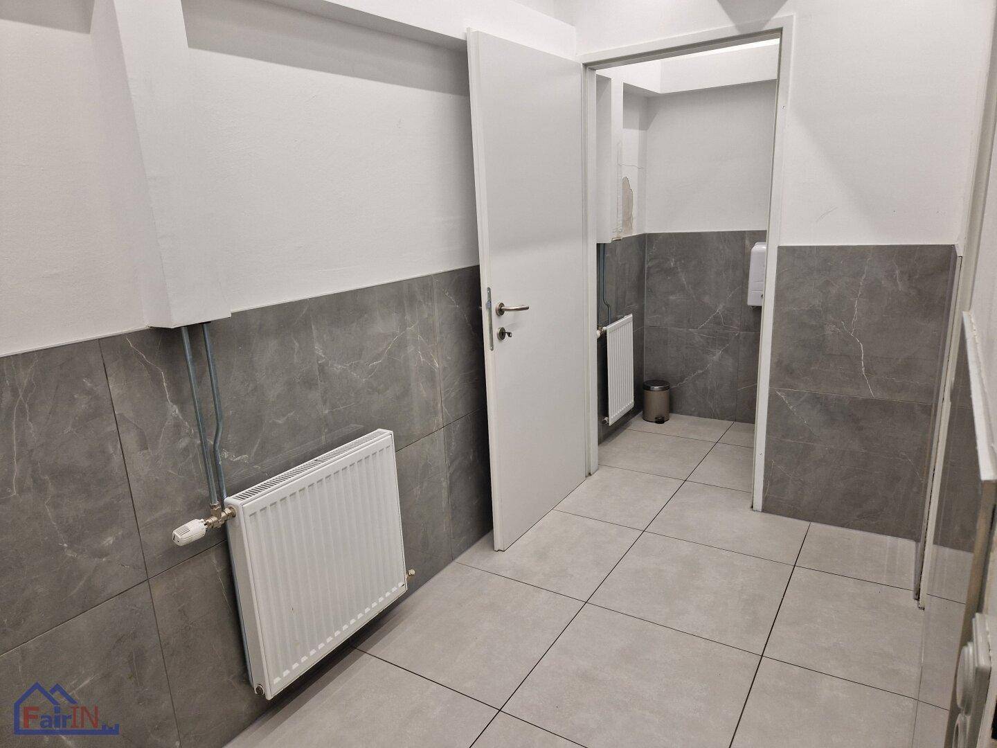 Toilettenraum mit Heizkörper und grauen Fliesen, bietet einfachen Zugang und Funktionalität.