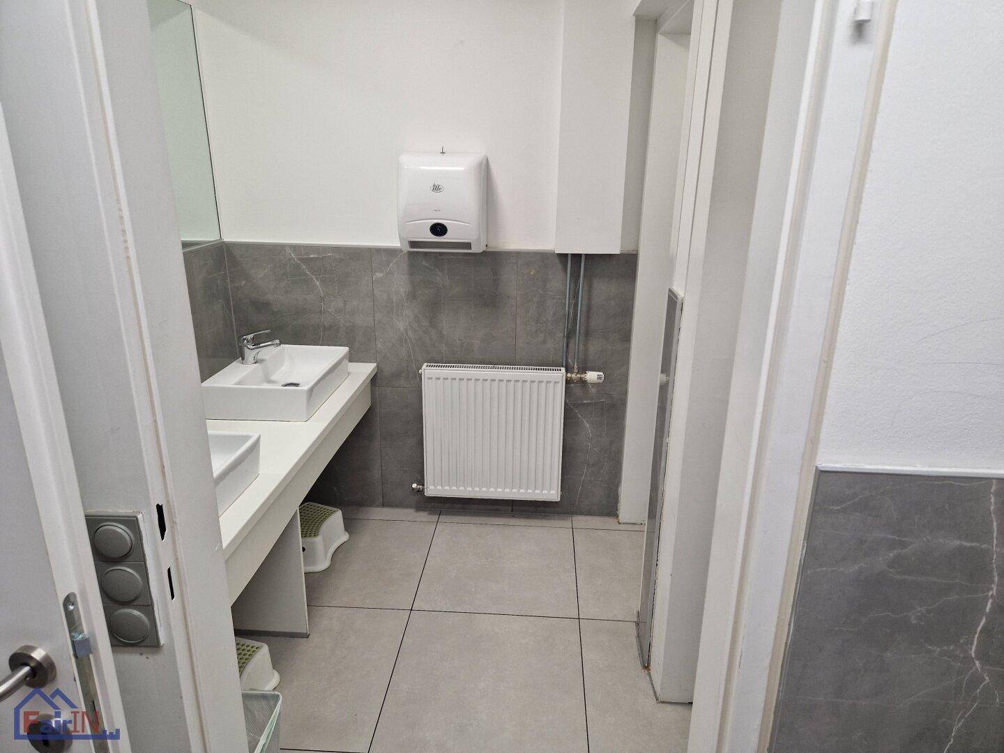Badezimmer mit zwei Waschbecken und Spiegel, ausgestattet mit modernen Armaturen und grauen Fliesen.