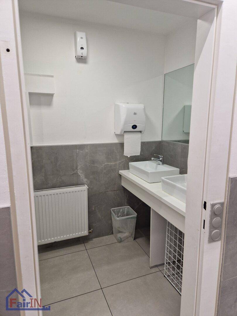 Badezimmer mit zwei Waschbecken und Handtuchspender, in einem hellen Raum mit grauen Fliesen.