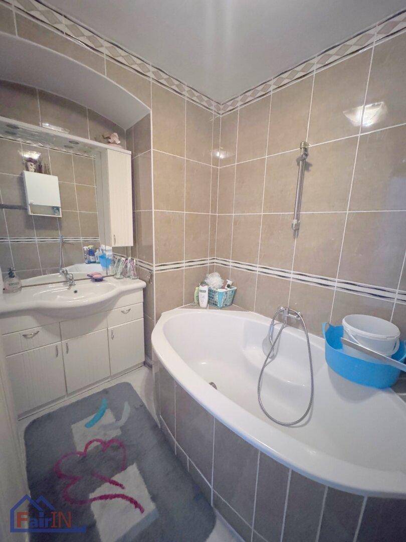 Gefliestes Badezimmer mit Badewanne, Waschbecken und Spiegelschrank, in beigen Farbtönen gehalten.