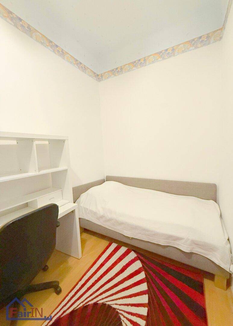 Schlafzimmer mit Einzelbett, Schreibtisch und einem auffälligen, farbenfrohen Teppich.