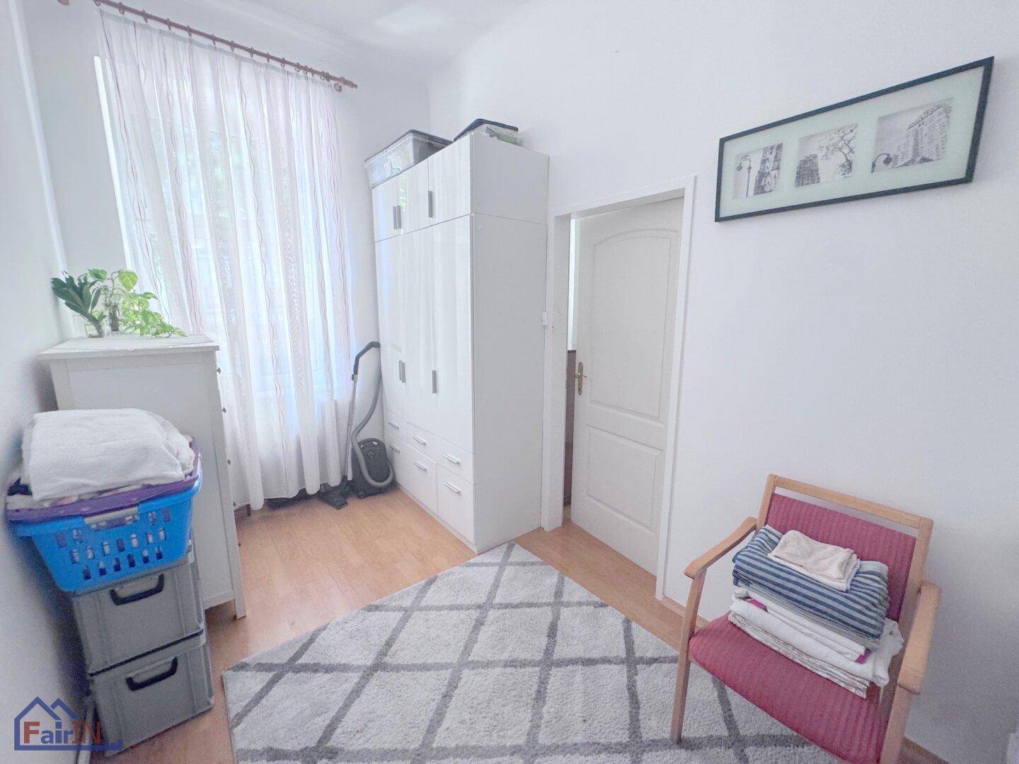 Schlafzimmer mit Schrank, Fenster und Wäschekorb, gut beleuchtet und funktional eingerichtet.