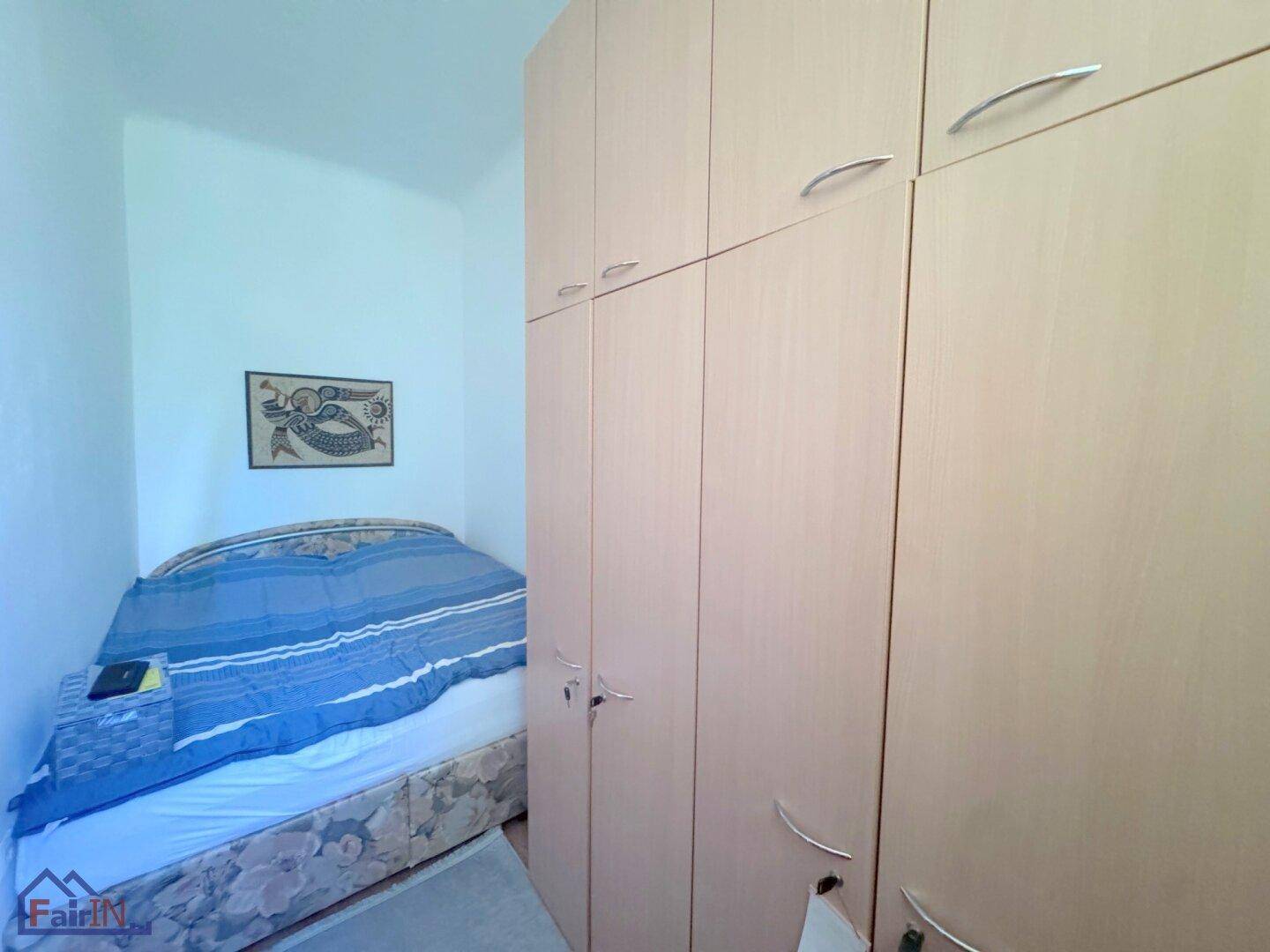 Schlafzimmer mit Einzelbett und hohen, hellen Einbauschränken, die viel Stauraum bieten.