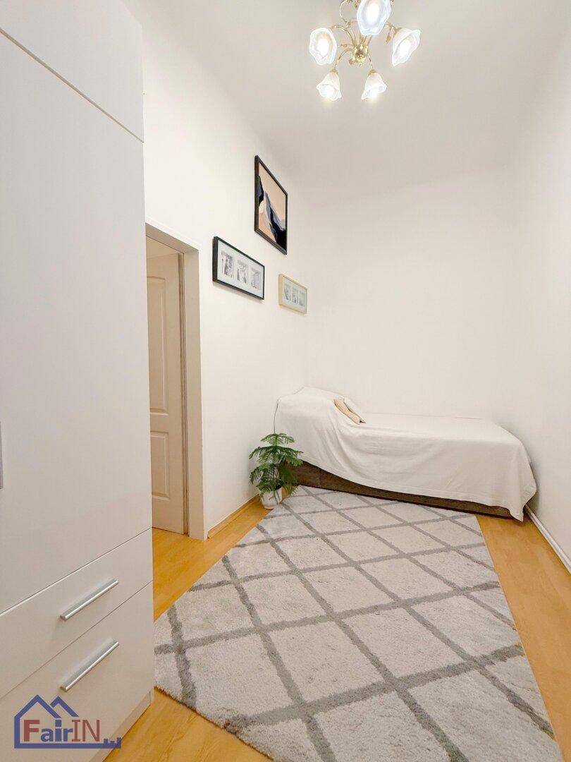 Helles Schlafzimmer mit Einzelbett, Teppich und schlichten Wanddekorationen, gut beleuchtet.