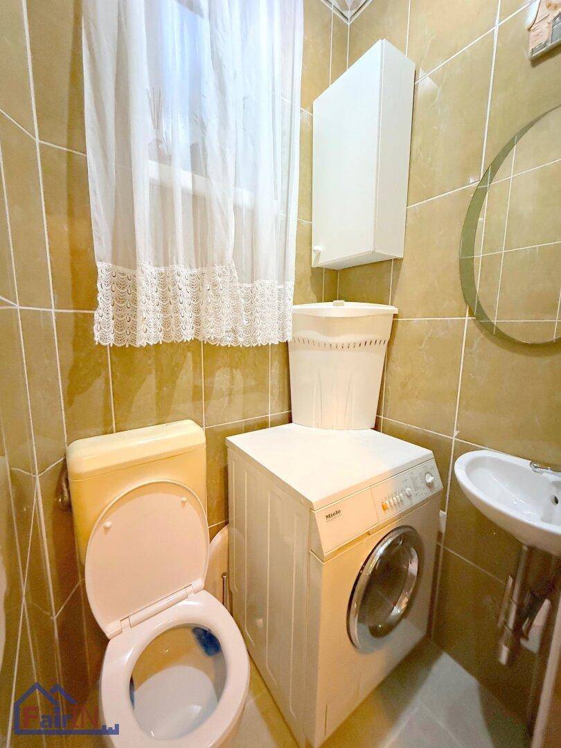 Kleines Badezimmer mit Toilette, Waschbecken und Waschmaschine, komplett gefliest.