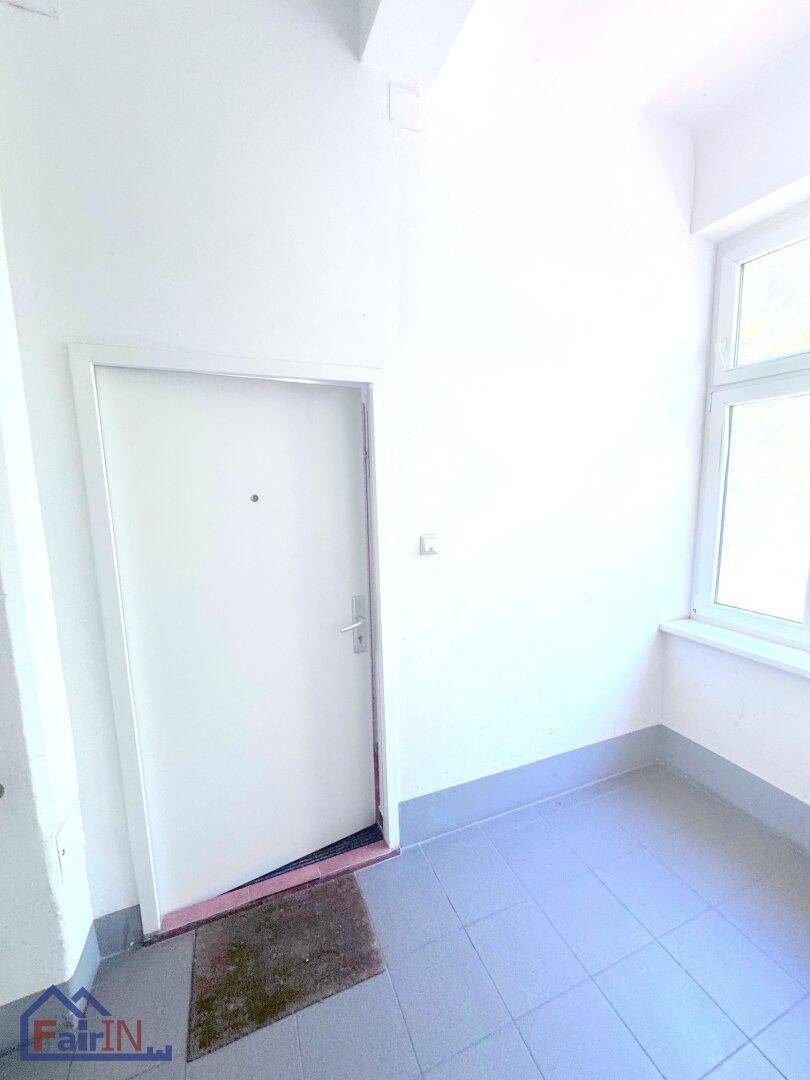 Heller Eingangsbereich mit Fliesenboden und Fenster, schlicht und funktional gestaltet.