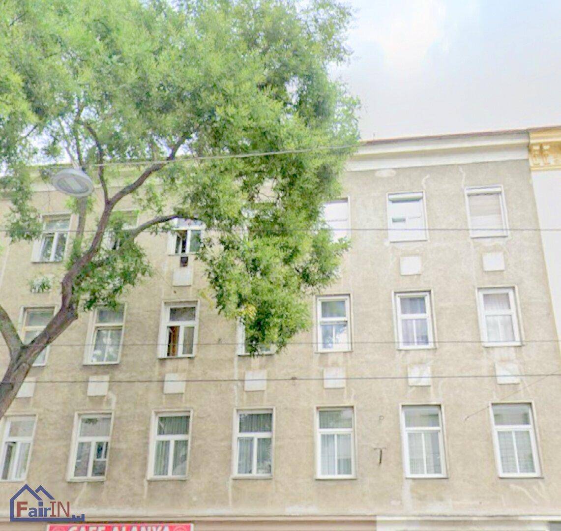Klassische Fassade eines Mehrfamilienhauses mit vielen Fenstern und einem großen Baum davor.