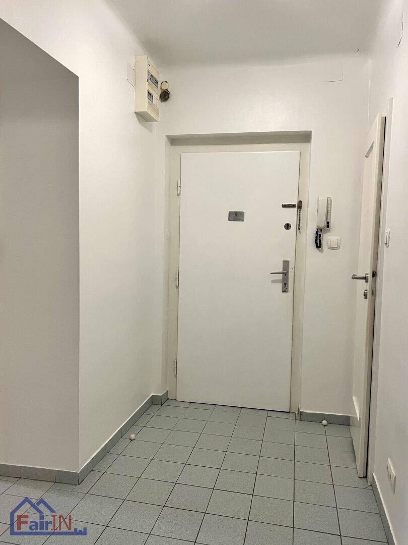 Eingangsbereich mit Fliesenboden, weißer Eingangstür und Gegensprechanlage.