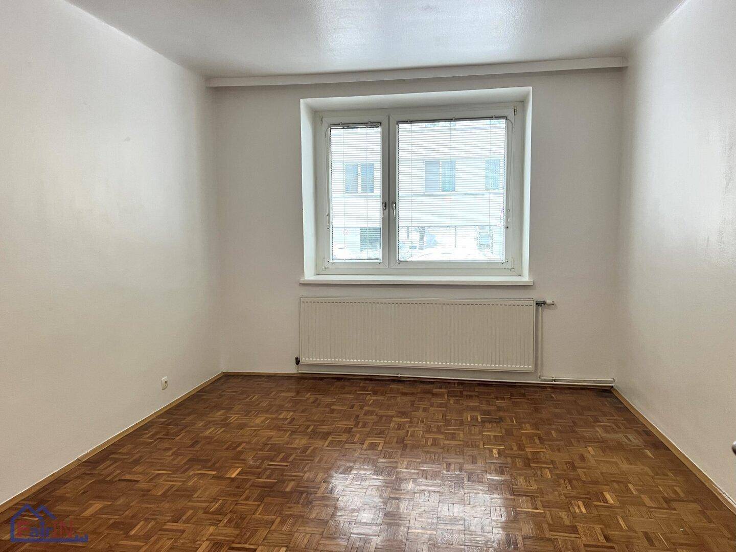 Helles Schlafzimmer mit klassischem Parkettboden und Fenster mit Jalousien.