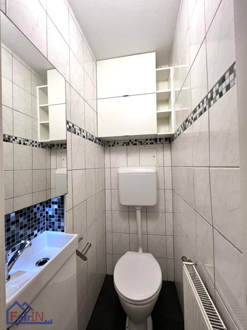 Kompaktes Gäste-WC mit weißen Fliesen, modernem Waschbecken und Heizkörper.