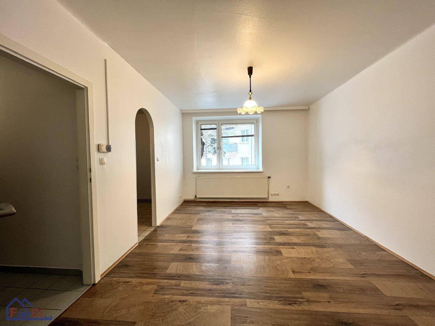 Geräumiger Wohnbereich mit Holzfußboden und Fenster mit Blick nach draußen.