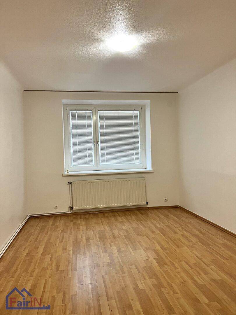 Helles Schlafzimmer mit klassischem Parkettboden und Fenster mit Jalousien.
