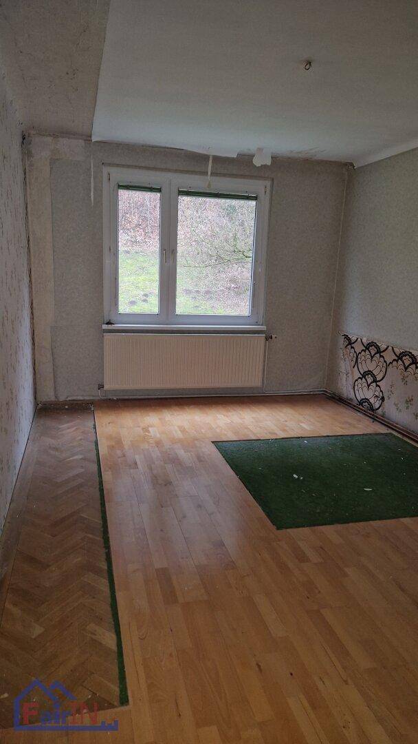Zimmer mit gemischtem Bodenbelag aus Parkett und Teppich sowie einem großen Fenster mit Blick ins Grüne.