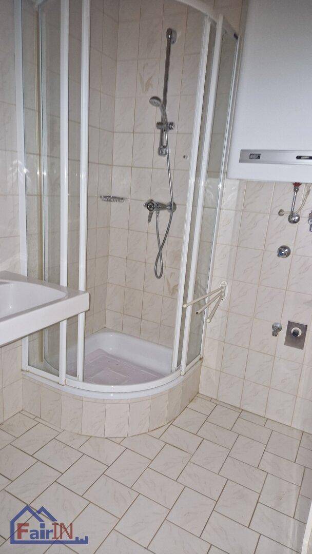 Helles Badezimmer mit Eckduschkabine, Fliesenboden und einem kleinen Waschbecken.