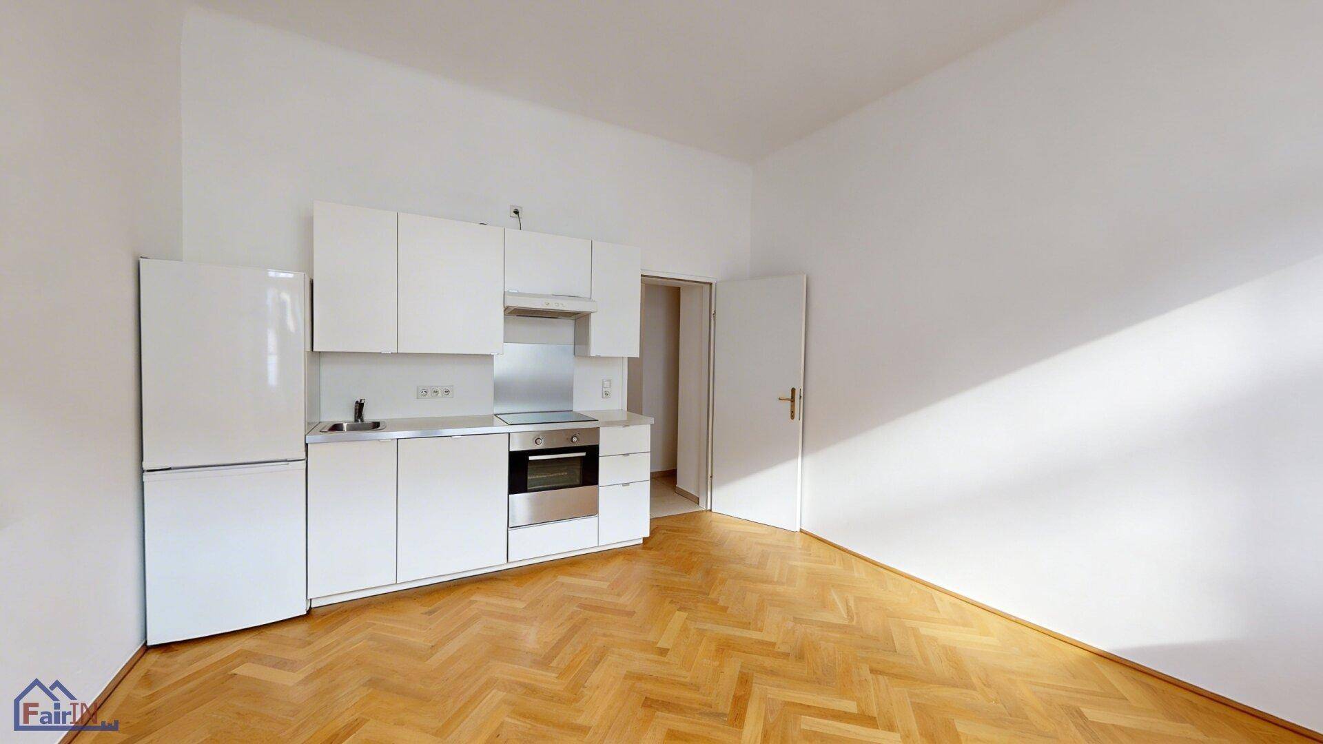 Moderne Einbauküche mit weißen Schränken und integrierten Geräten in einem hellen Raum mit Parkettboden.