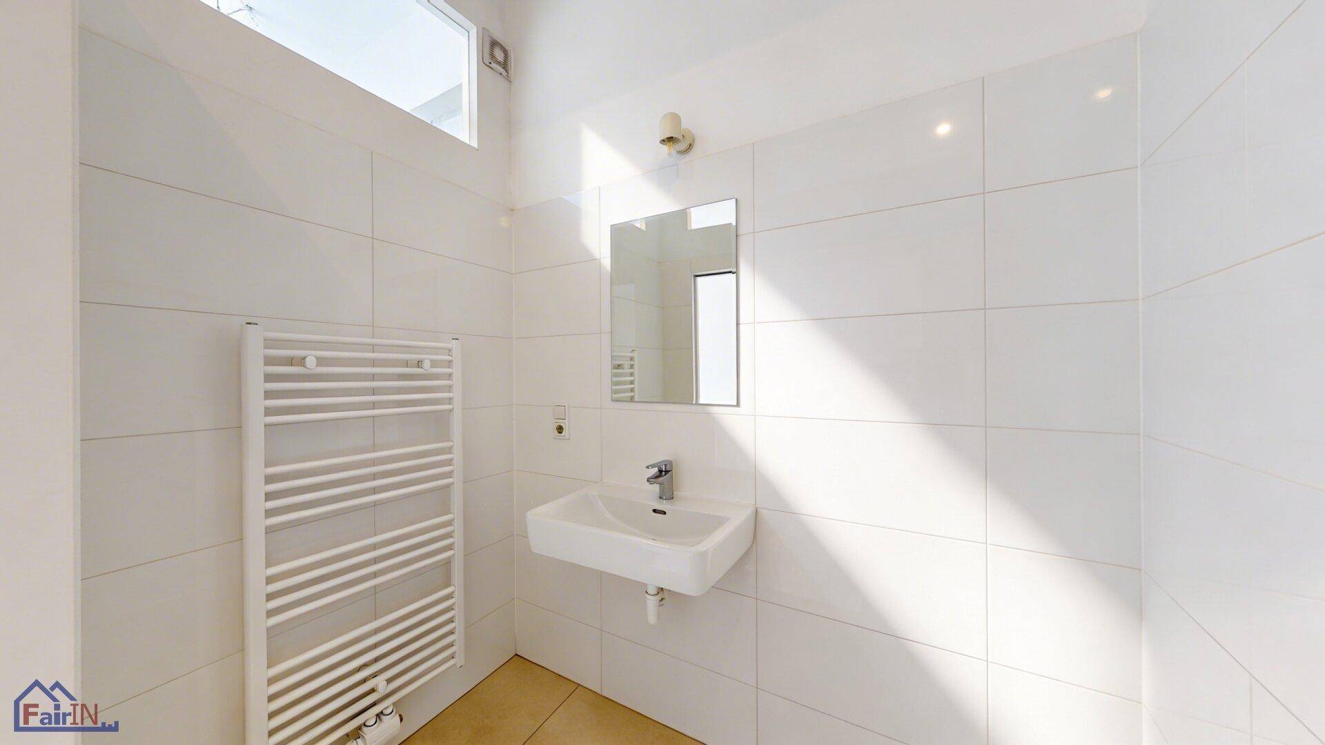 Helles Badezimmer mit weißen Fliesen, Einzelwaschbecken, beheiztem Handtuchhalter und Fenster.