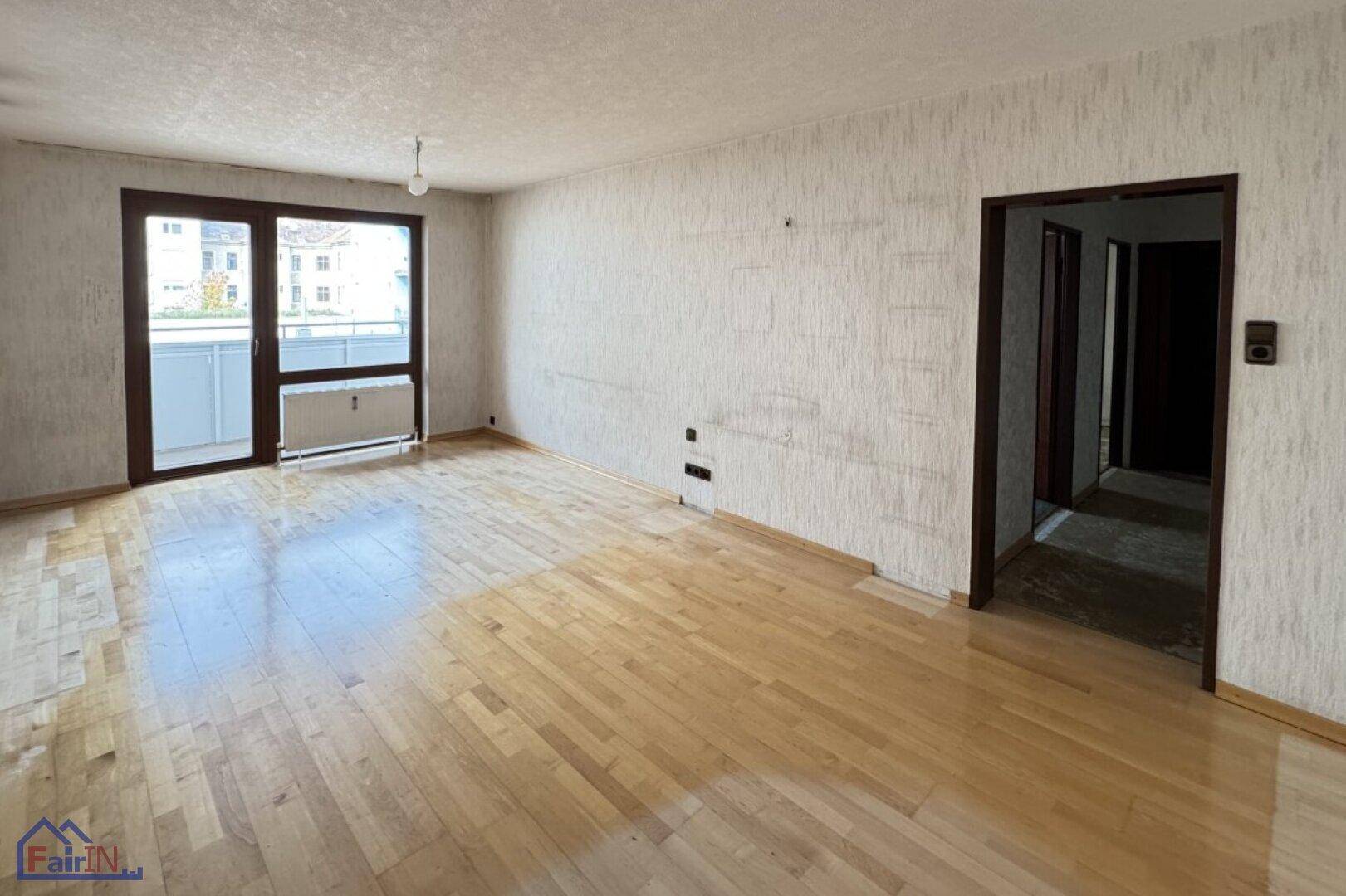 Leeres Wohnzimmer mit hellem Parkettboden und Zugang zu einem Balkon, bereit zur Renovierung.