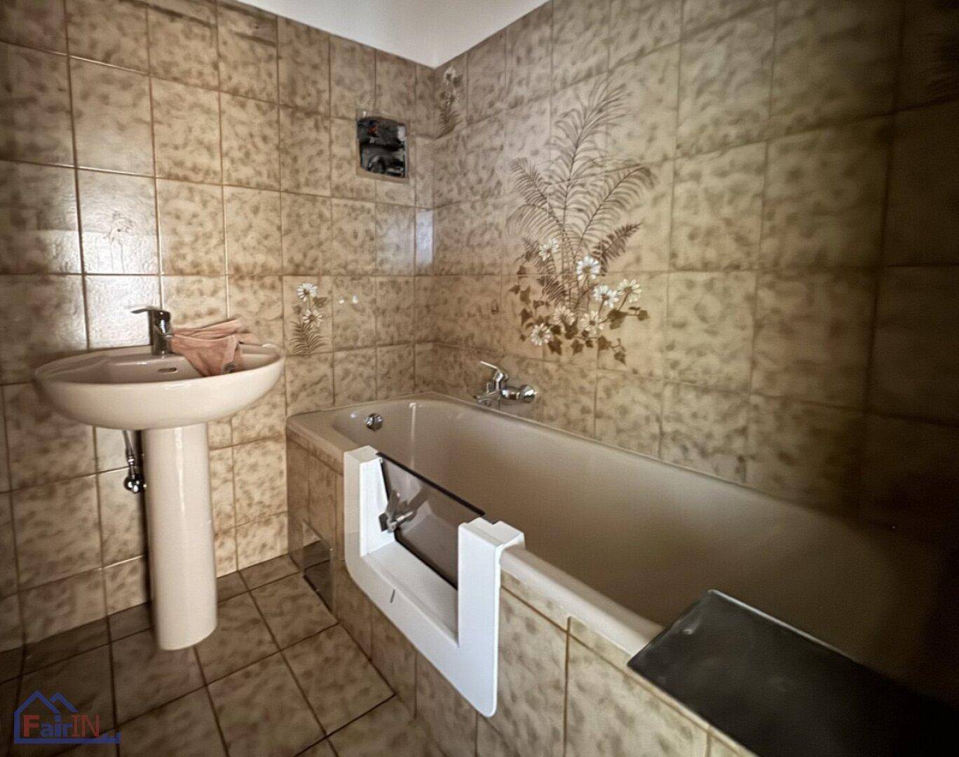 Badezimmer im Stil der 80er Jahre mit Badewanne, Waschbecken und braunen Wandfliesen.