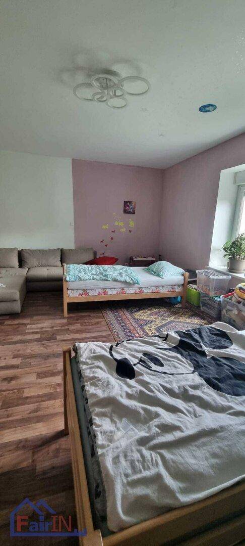Kinderzimmer mit zwei Einzelbetten, einem Sofa und einem Fenster, das viel Tageslicht hereinlässt.