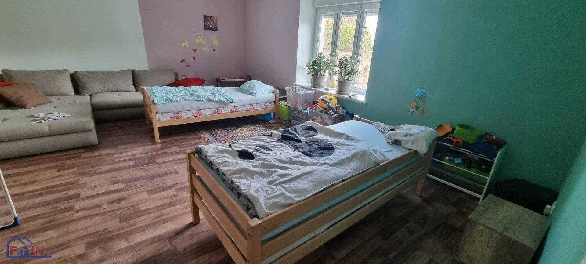 Helles Kinderzimmer mit zwei Einzelbetten, einem Sofa und einem Fenster, das den Raum erhellt.