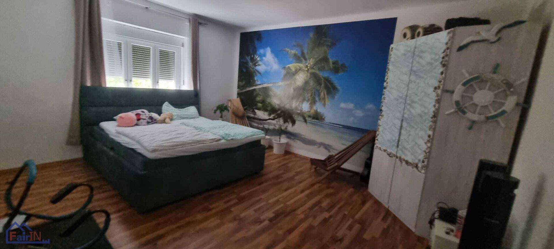 Schlafzimmer mit großem Bett, Kleiderschrank und einer Wandtapete, die eine tropische Strandlandschaft zeigt.