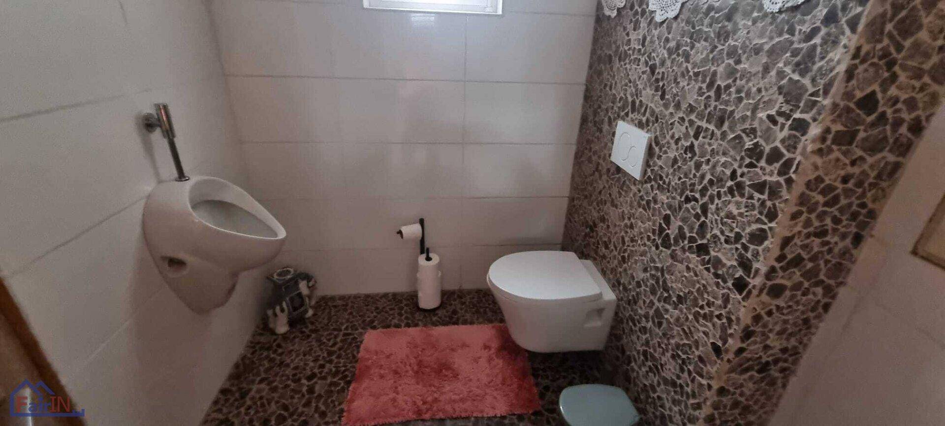 Modernes Gäste-WC mit Urinal, wandhängendem WC und dekorativen Fliesen in Steinoptik.