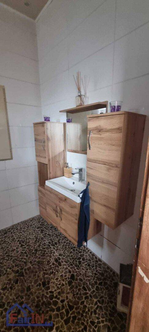 Badezimmer mit modernem Waschtisch, Holzschränken und dekorativen Bodenfliesen in Steinoptik.