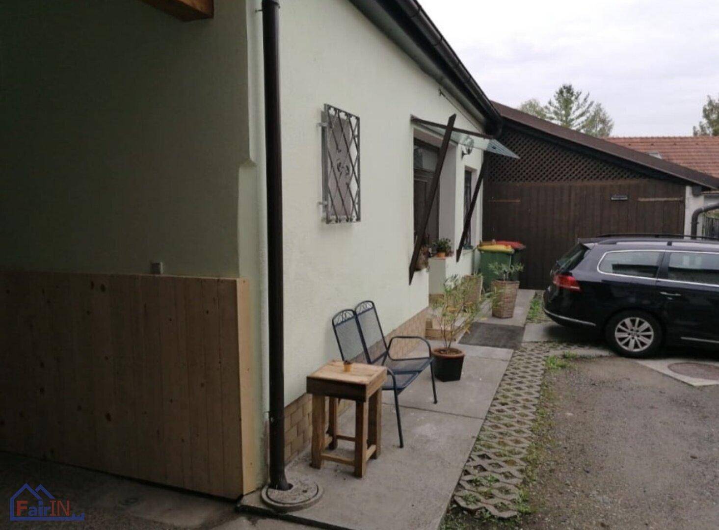 Seitenansicht des Hauses mit einer kleinen Sitzecke im Freien und einem geparkten Auto neben der Garage.