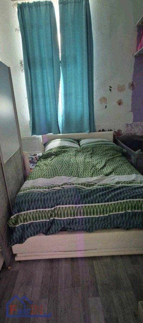 Schlafzimmer mit Bett, farbiger Bettwäsche und einem Fenster mit blauen Vorhängen.