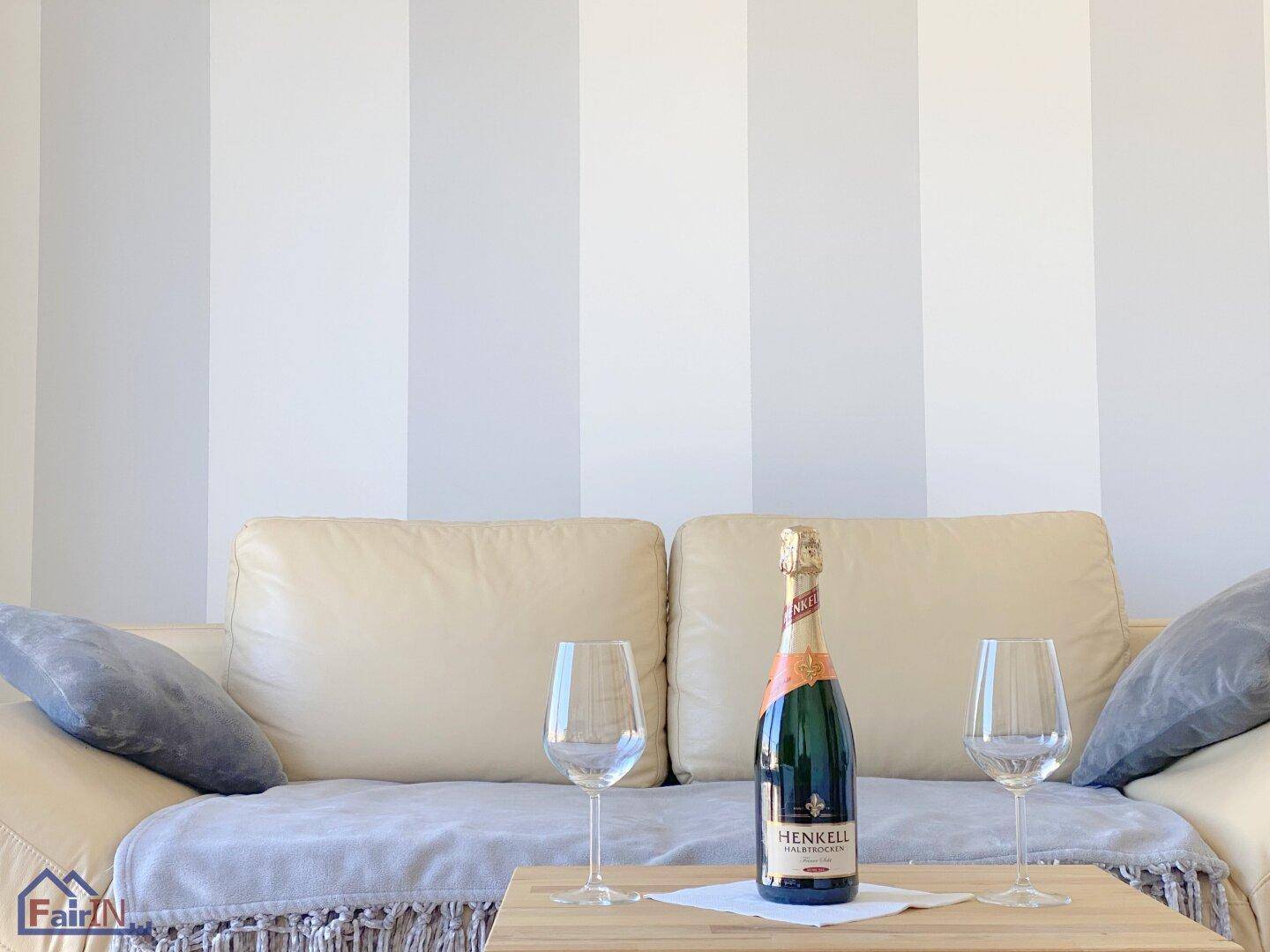 Gemütliches Wohnzimmer mit beigem Sofa, gestreifter Wand und einer Flasche Champagner.