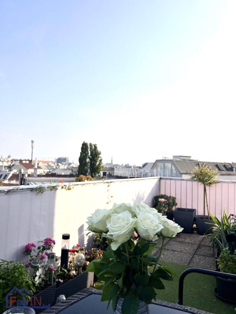 Sonnige Terrasse mit üppiger Bepflanzung und einem Strauß weißer Rosen im Vordergrund.