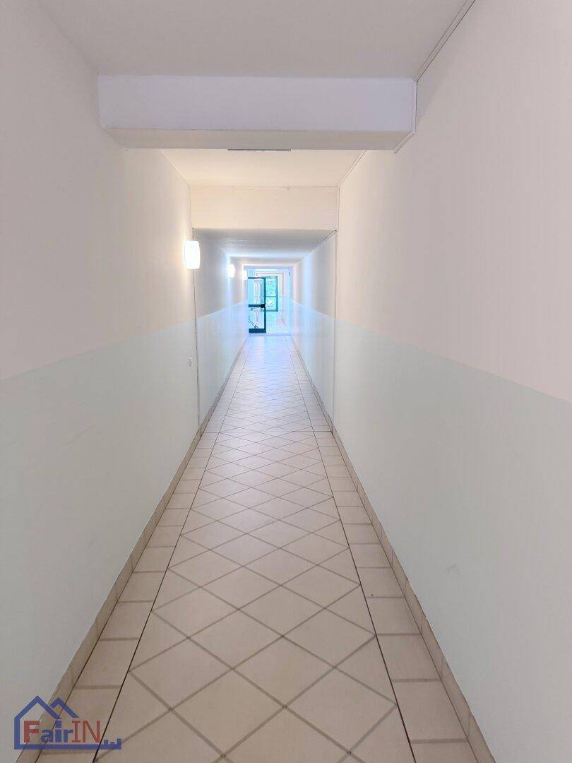 Langer Gemeinschaftsflur mit Fliesenboden und zweifarbigen Wänden in einem Mehrfamilienhaus.