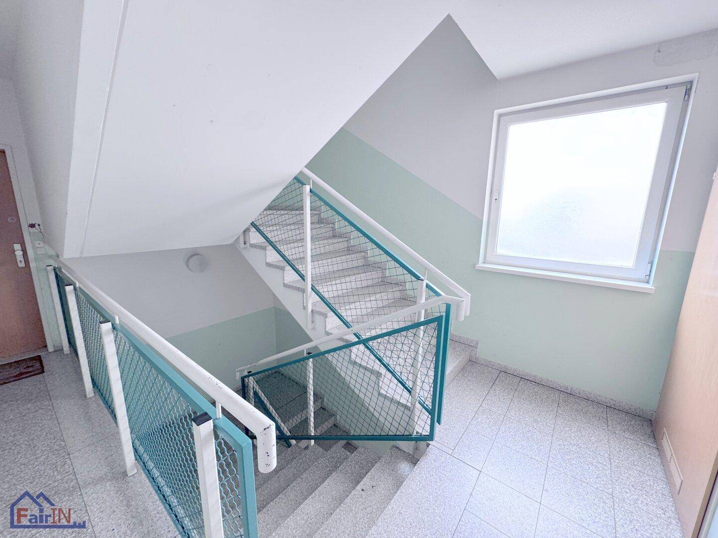 Treppenhaus mit grünen Metallgeländern und Fliesenboden in einem Mehrfamilienhaus.