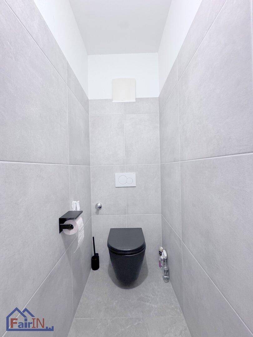 Modernes Gäste-WC mit grauen Fliesen und einer stilvollen schwarzen Wandtoilette.