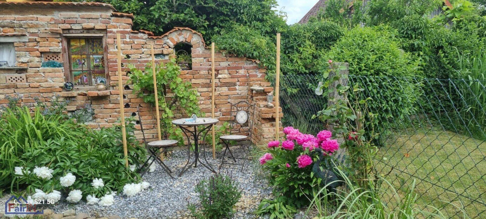 Blühender Gartenbereich mit bunten Blumen, Kies und einer charmanten Sitzecke an der Ziegelmauer.
