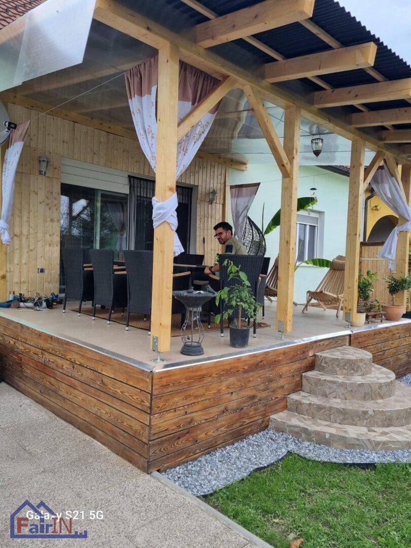 Überdachte Holzterrasse mit großem Esstisch und Stühlen, ideal für Mahlzeiten im Freien und Entspannung.